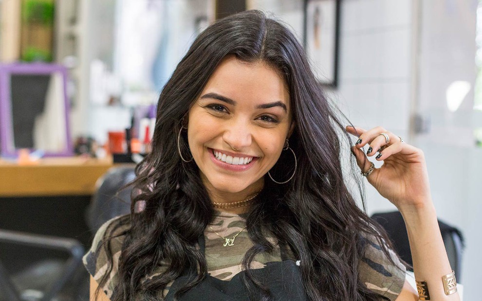 Talita Younan em cena de Malhação - Viva a Diferença: atriz sorri para câmera e segura uma mecha de cabelo com as pontas dos dedos