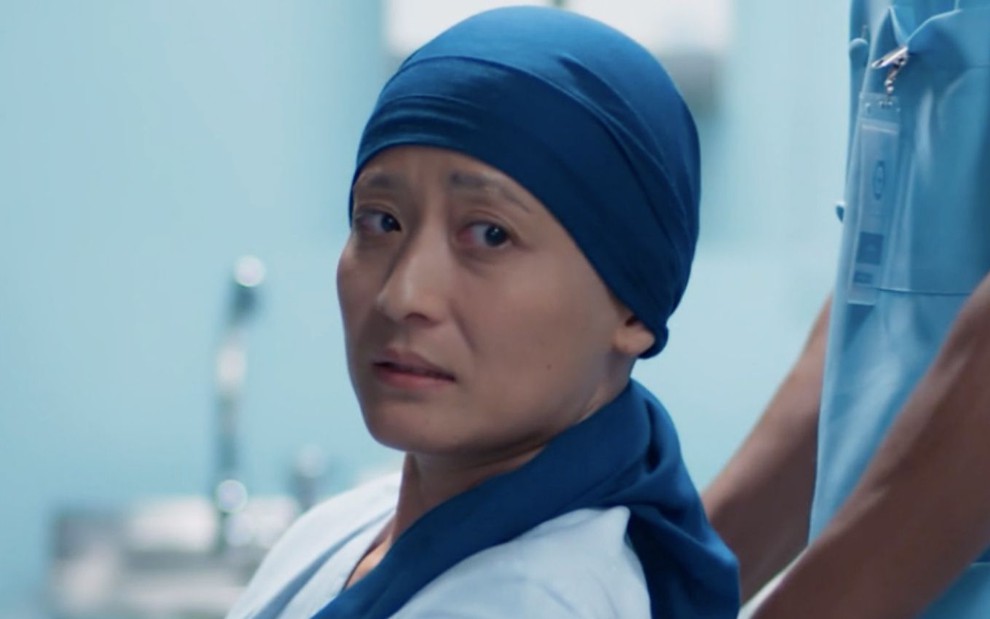 A personagem Mitsuko (Lina Agifu) olha em estado de choque com uma bandana na cabeça em cena da novela Malhação - Viva a Diferença
