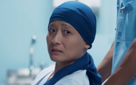 A personagem Mitsuko (Lina Agifu) olha em estado de choque com uma bandana na cabeça em cena da novela Malhação - Viva a Diferença
