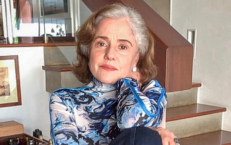 Marieta Severo em foto de divulgação para o site da Globo: sentada e com os braços cruzados, atriz usa blusa estampada e calça azul