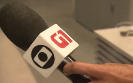 Imagem do microfone da Globo, com os logos da Globo e do G1, na mão de uma pessoa na Redação