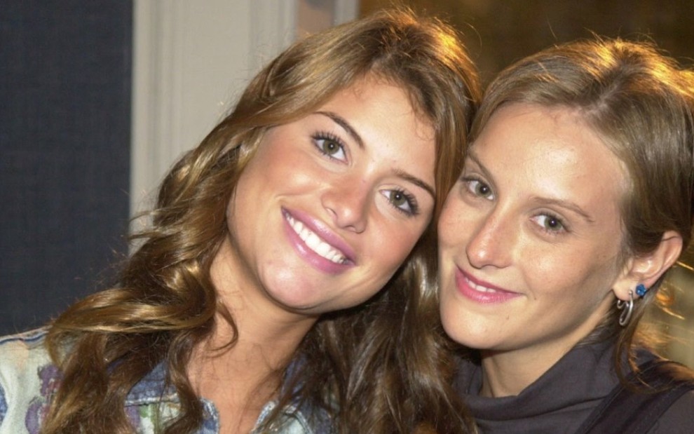 As atrizes Alinne Moraes (Rafaela) e Paula Picarelli (Clara) sorriem abraçadas como as personagens de Mulheres Apaixonadas