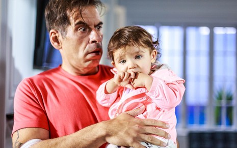 De camiseta vermelha, Leandro Hassum segura bebê em cena do filme Não se Aceitam Devoluções