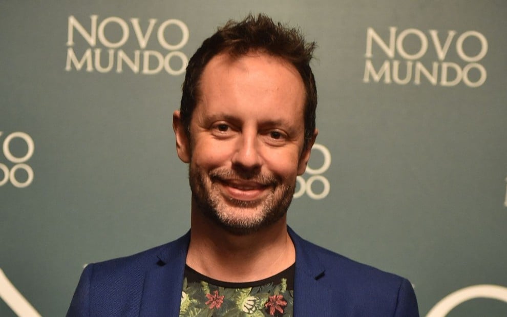 Alessandro Marson em festa de Novo Mundo (2017), autor sorri para a câmera, usa camiseta florida e blazer azul marinho