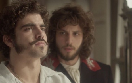 O ator Caio Castro em primeiro plano como Pedro olha para cima, enquanto Chay Suede, o Joaquim, está ao fundo em cena de Novo Mundo