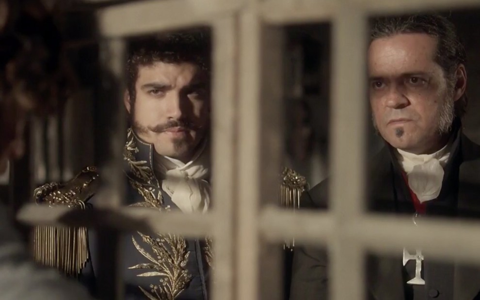 O ator Caio Castro e Felipe Camargo, como Caio e Bonifácio, atrás de uma grade em cena de Novo Mundo