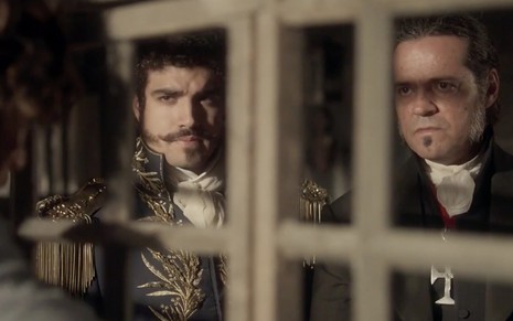 O ator Caio Castro e Felipe Camargo, como Caio e Bonifácio, atrás de uma grade em cena de Novo Mundo