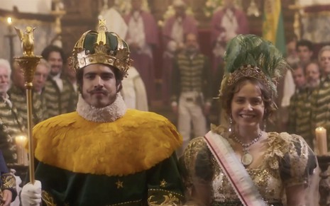 Os atores Caio Castro e Leticia Colin com coroas e cetros, além de roupas de gala, cercado por populares como Pedro e Leopoldina em cena de Novo Mundo