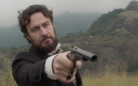 O ator Gabriel Braga Nunes segura um revólver caracterizado como Thomas em cena da novela Novo Mundo