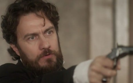 O ator Gabriel Braga Nunes segura um revólver caracterizado como o Thomas de Novo Mundo