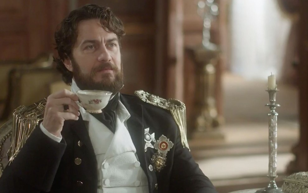 Thomas (Gabriel Braga Nunes) sentado, tomando uma xícara de chá em cena de Novo Mundo