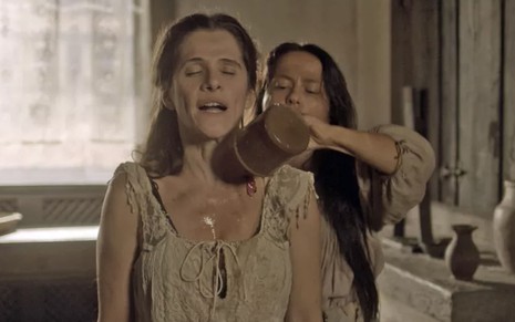 A atriz Ingrid Guimarães, a Elvira, em uma tina, leva um banho de caneca dado por Vivianne Pasmanter, a Germana, em cena de Novo Mundo