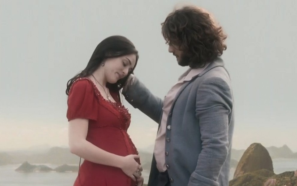 A atriz Isabelle Drummond segura a barriga, grávida, caracterizada como a Anna enquanto Chay Suede, o Joaquim, passa a mão pelos seus cabelos em cena de Novo Mundo