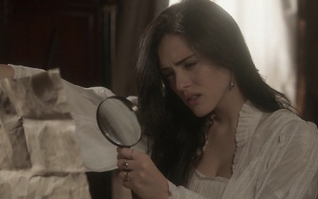 A atriz Isabelle Drummond com um mapa na mão esquerda e uma lupa na mão direita procura por algo caracterizada como Anna em cena de Novo Mundo