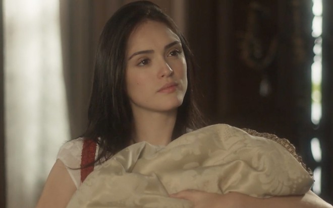 A atriz Isabelle Drummond segura um bebê no colo caracterizada como a Anna em cena de Novo Mundo