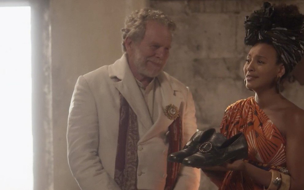 O ator Jonas Bloch como Wolfgang observa Sheron Menezzes caracterizada de Diara segurar sapatos masculinos em cena de Novo Mundo