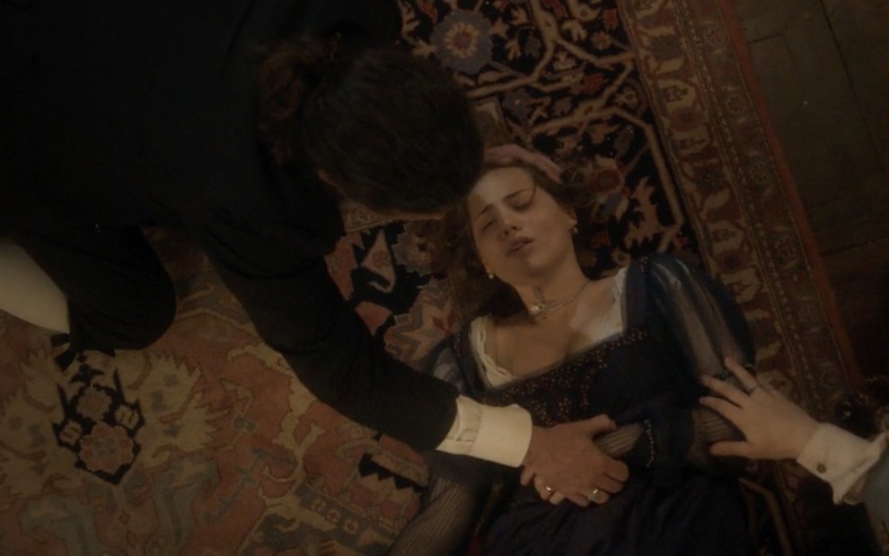 A atriz Leticia Colin caracterizada como Leopoldina está desmaiada em um tapete enquanto dois homens a acodem em cena de Novo Mundo