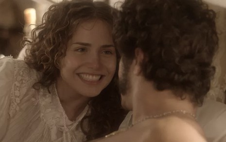 A atriz Letícia Colin à esquerda, deitada na cama, com uma camisola do século 19, caracterizada como Leopoldina, olha para Caio Castro, que está de costas como Pedro, em cena de novo Mundo