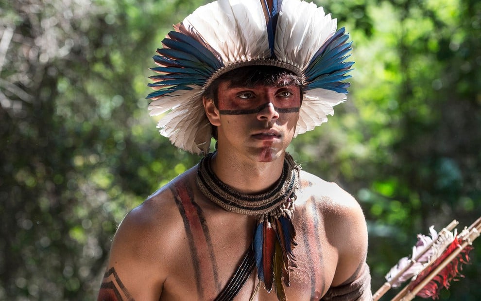 O ator Felipe Simas, seminu, com pintura indígena e um cocar como o índio Piatã em cena de Novo Mundo