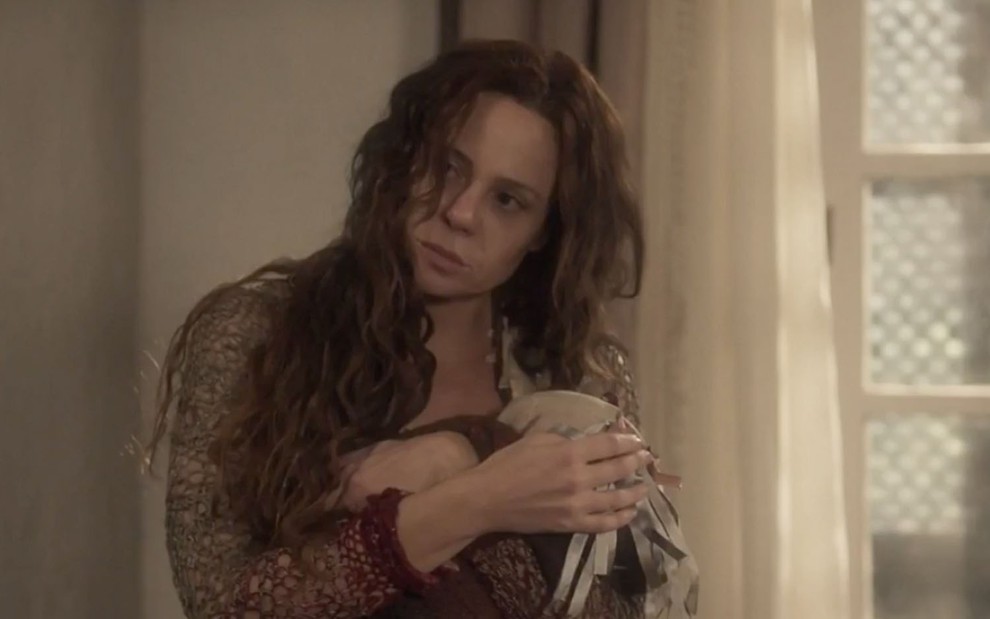 A atriz Vanessa Gerbelli segura um amontado de trapos caracterizada como a Amália em cena de Novo Mundo