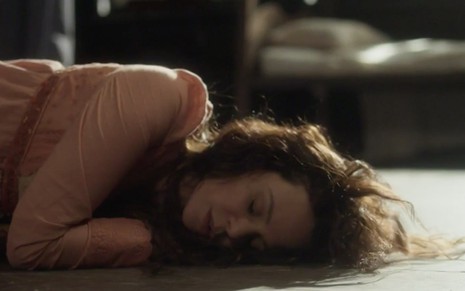 A atriz Vanessa Gerbelli caracterizada como Amália está caída no chão, como que desmaiada, em cena de Novo Mundo
