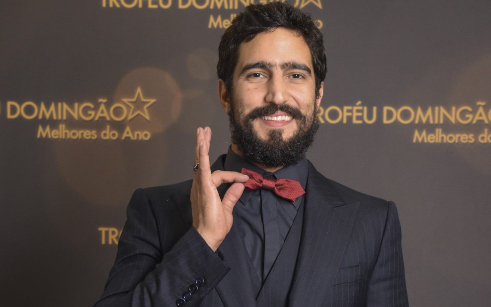 O ator Renat Góes segura gravata borboleta vermelha em gravação de premiação da Globo