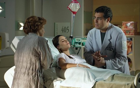 A atriz Fernanda Vasconcellos deitada em uma cama, e o ator Thiago Lacerda ao seu lado em pé, em cena como Ana e Lúcio em A Vida da Gente