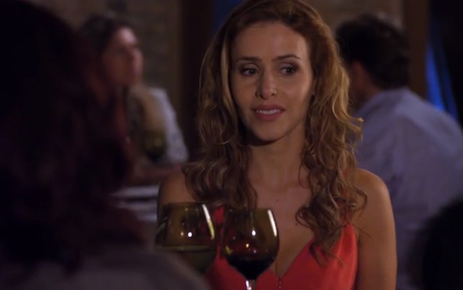 A atriz Leona Cavalli, sentada em uma mesa de restaurante, com expressão de desagrado, durante cena como Celina de A Vida da Gente