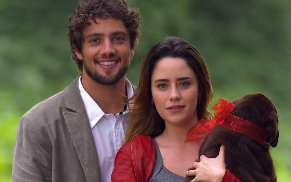 Os atores Rafael Cardoso e Fernanda Vasconcellos, lado a lado, e a atriz segura um cachorro em cena de A Vida da Gente
