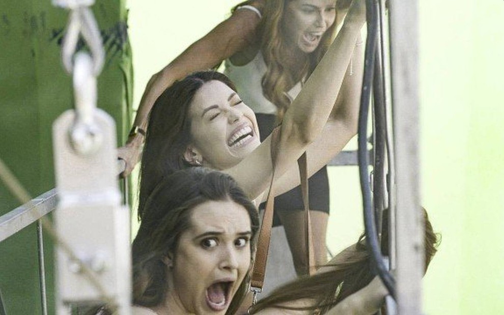As atrizes Deborah Secco, Juliana Paiva e Vitória Strada, com expressão de medo em cima de um andaime, em cena como Alexia, Luna e Kyra em Salve-se Quem Puder