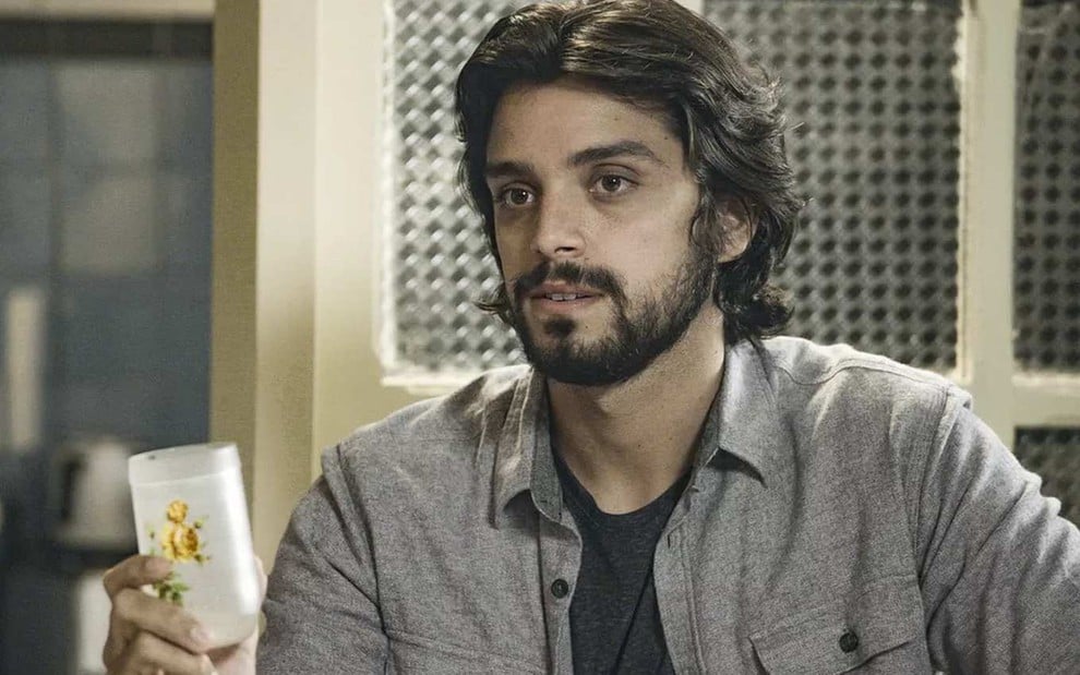 O ator Rodrigo Simas, segurando um copo, em cena como Alejandro em Salve-se Quem Puder