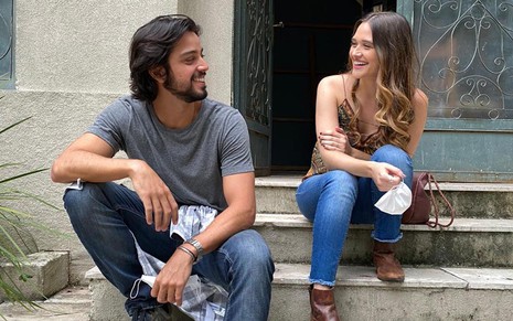 O ator Rodrigo Simas olha para Juliana Paiva durante gravação de cena de Salve-se Quem Puder; eles estão sentados em uma escada