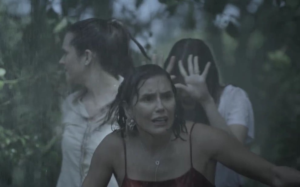 A atriz Juliana Paiva grava cena da novela Salve-se Quem Puder com blusa clara juntamente com Deborah Secco e Vitória Strada, que cobre o rosto com mão por causa da chuva