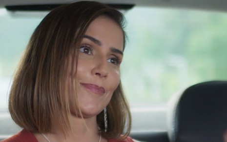 A atriz Deborah Secco sorri em cena em que está no banco de trás de um automóvel na novela Salve-se Quem Puder