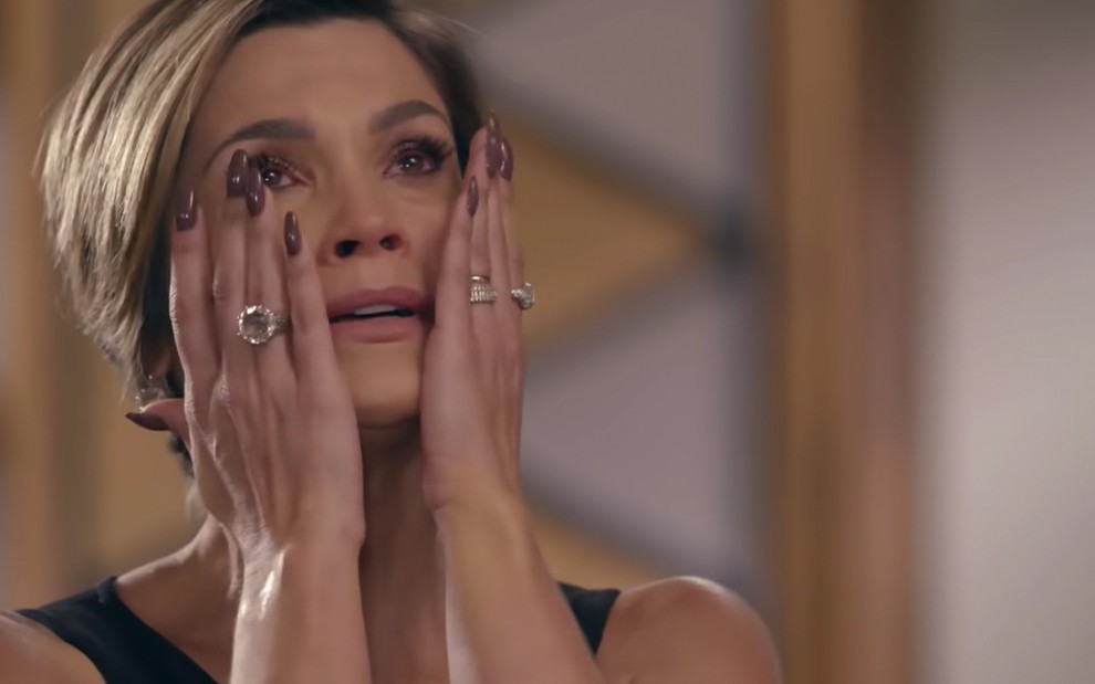 A atriz Flávia Alessandra como Helena chora e leva as mãos ao rosto para secar as lágrimas em cena de Salve-se Quem Puder