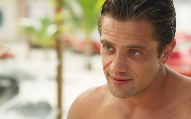 O ator Rafael Cardoso, com um sorriso no rosto e sem camisa, em sequência da novela Salve-se Quem Puder, da TV Globo