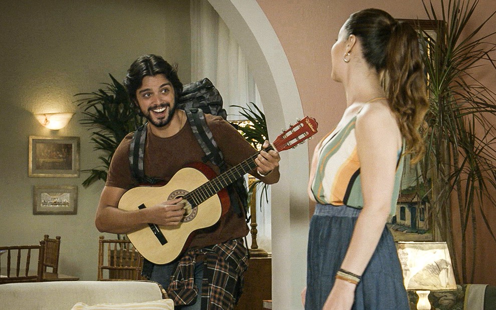 Com uma mochila nas costas e um violão na mão, Rodrigo Simas está como Alejandro e canta para Nina Frosi, a Gabi, que está de costas em cena de Salve-se Quem Puder