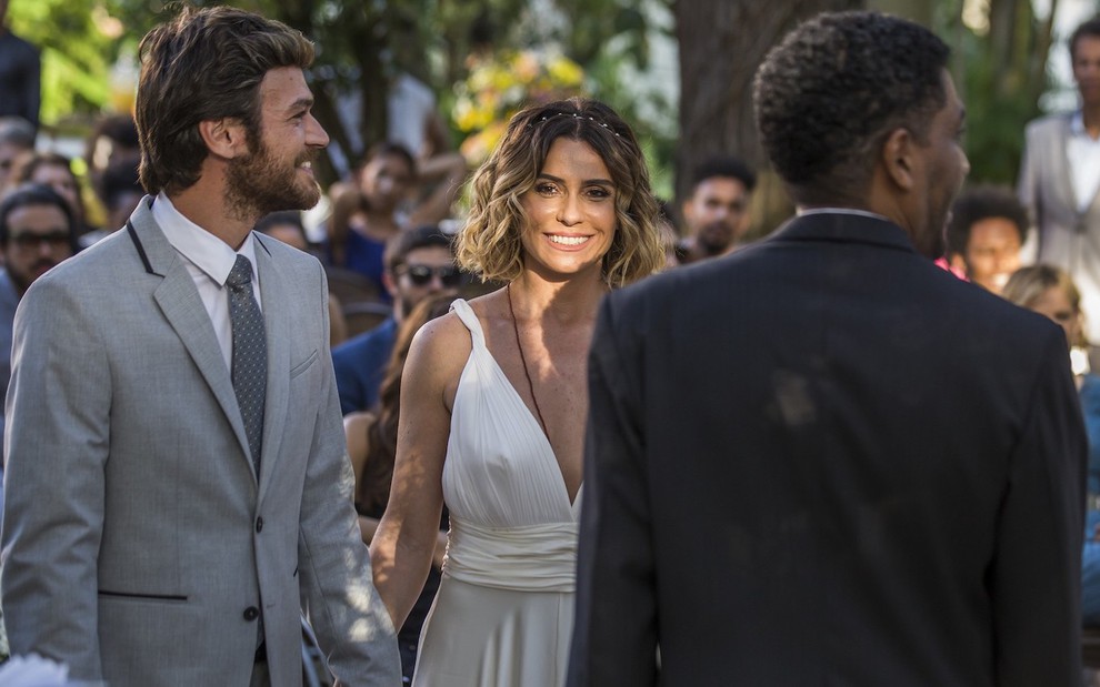 Emilio Dantas usa terno e gravata e Giovanna Antonelli vestido branco em cena de Segundo Sol com ator negro de costas