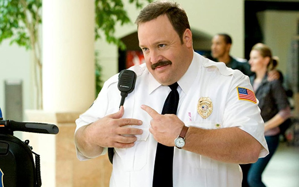 Kevin James é Paul Blart em Segurança de Shopping: ele aponta para um rádio em seu ombro