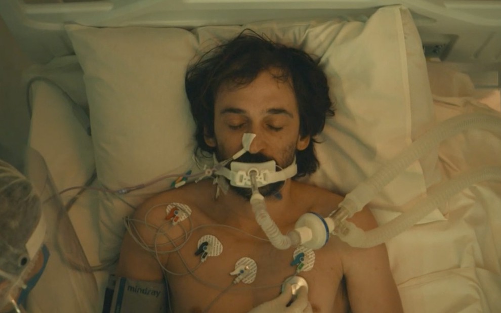 O ator Julio Andrade deitado em camisa em uma leito hospitalar, entubado e com eletrodos colados no corpo como doutor Evandro de Sob Pressão: Plantão Covid