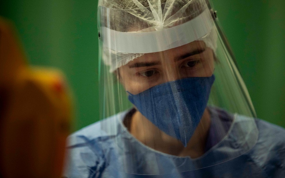 A atriz Marjorie Estiano com um face-shield, máscara N-5 e um capote azul como a médica Carolina em cena de Sob Pressão: Plantão Covid