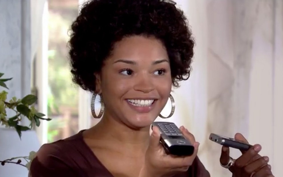 Juliana Alves em cena de Ti Ti Ti: caracterizada como Clotide, atriz segura telefone e sorri para o horizonte