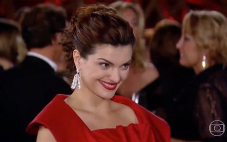 A atriz Mayana Neiva sorri em cena de Ti Ti Ti, na qual sua prsonagem Desirée usa um vestido vermelho de alta-costura