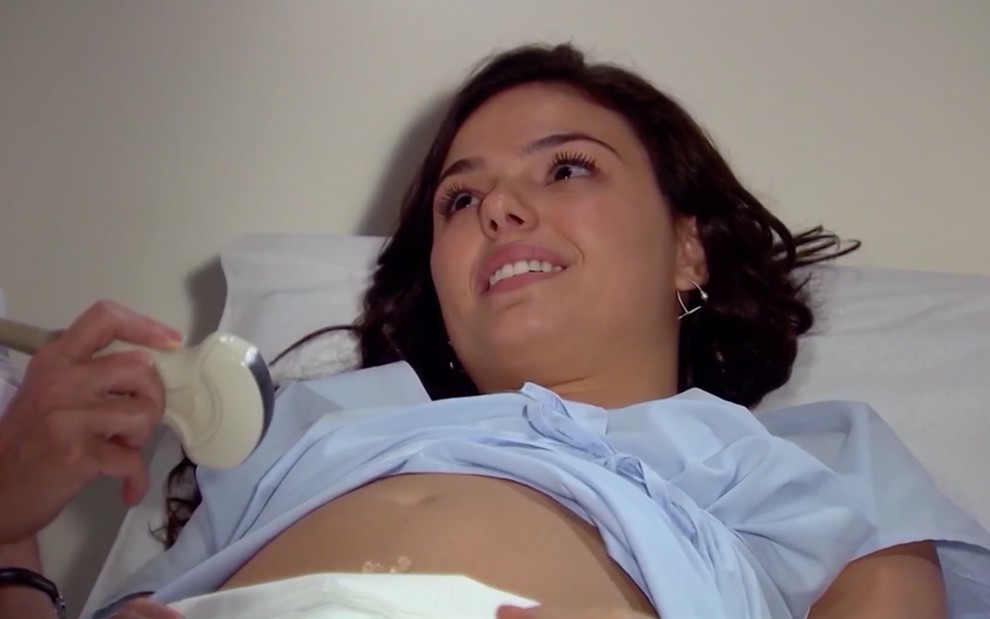 Isis Valverde em cena de Ti Ti Ti: caracterizada como Marcela, atriz está em maca de hospital e olha com emoção para algo fora do quadro