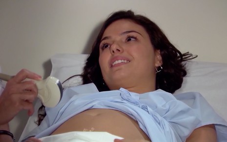 Isis Valverde em cena de Ti Ti Ti: caracterizada como Marcela, atriz está em maca de hospital e olha com emoção para algo fora do quadro