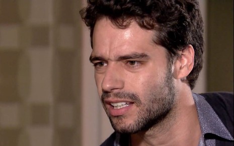 Guilherme Winter em cena de Ti Ti Ti: caracterizado com Renato, ator olha para baixo com expressão de seriedade