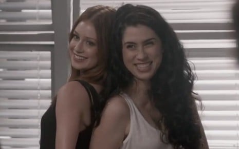 As atrizes Marina Ruy Barbosa e Olívia Torres em cena de Totalmente Demais: Marina sorri e usa regata preta, já Olivia usa regata branca e também sorri 