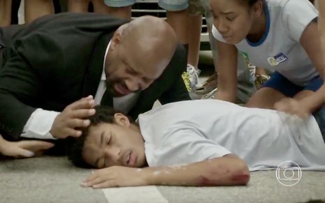 Ailton Graça agacha no chão próximo a Juan Paiva, que é cercado por outros atores em cena de atropelamento de Totalmente Demais