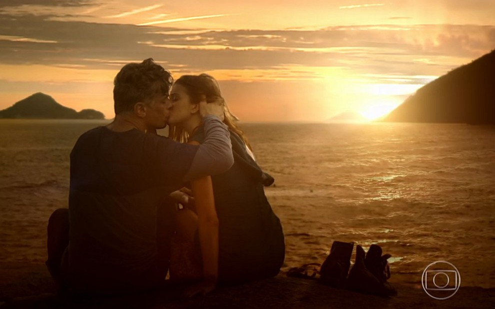 Arthur (Fabio Assunção) e Eliza (Marina Ruy Barbosa) se beijam sentados na praia diante do pôr do sol em cena de Totalmente Demais