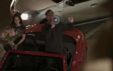 Fabio Assunção, interpretando Arthur, na novela Totalmente Demais, em cima de um carro conversível, falando em um megafone